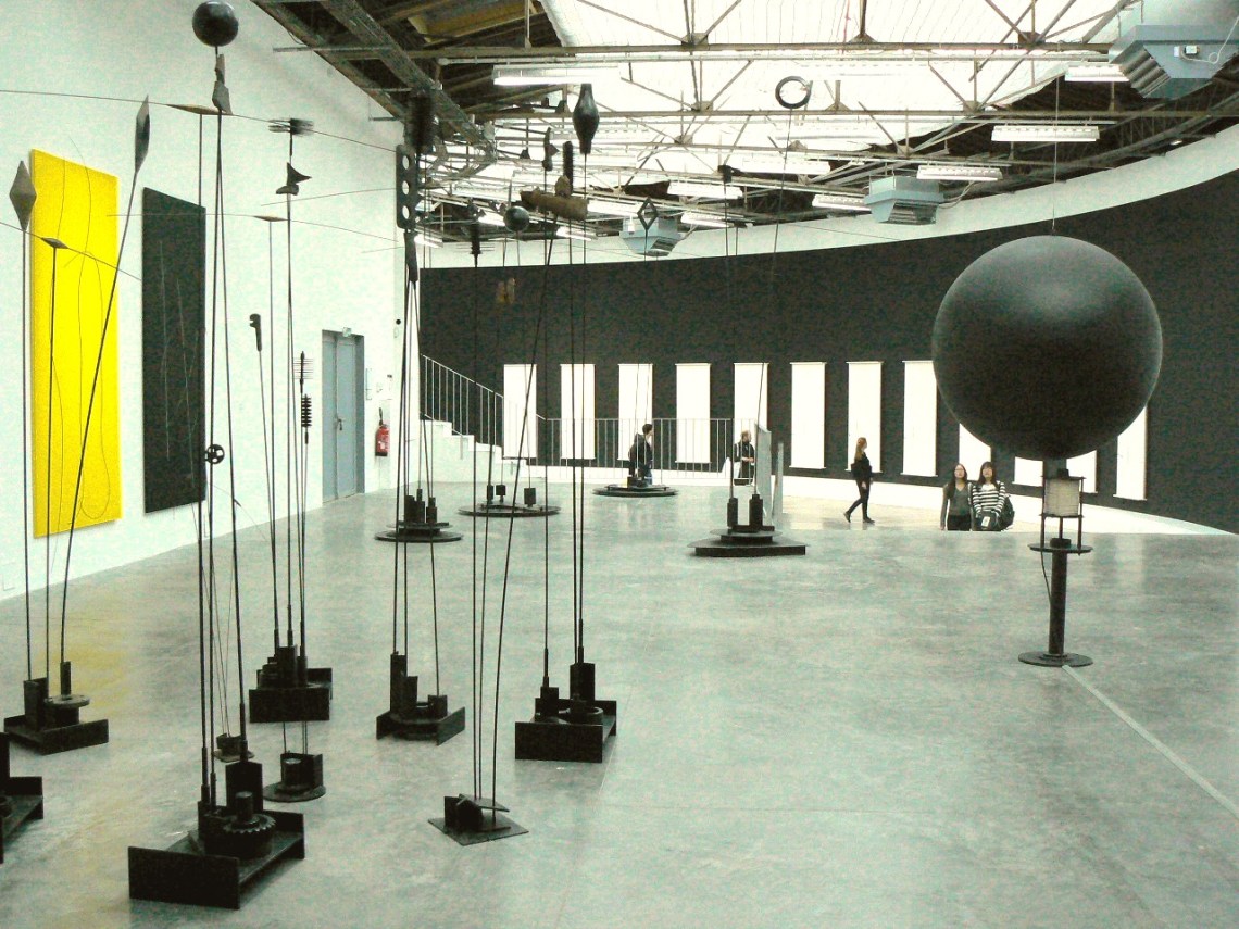 Az előtérben a Signal à Quatre Bras (1967, fém, 320 × 320 × 49 cm, Laffanour Galerie Downtown, Párizs), továbbá a Signal Lumineux (1976, fém, elektronika, 240 cm, Laffanour Galerie Downtown, Párizs), a háttérben a 6 Musicales (2000–2003, festett fa, áramkör, kábel, fém, 257 × 100 cm, Takis Foundation, Athén).